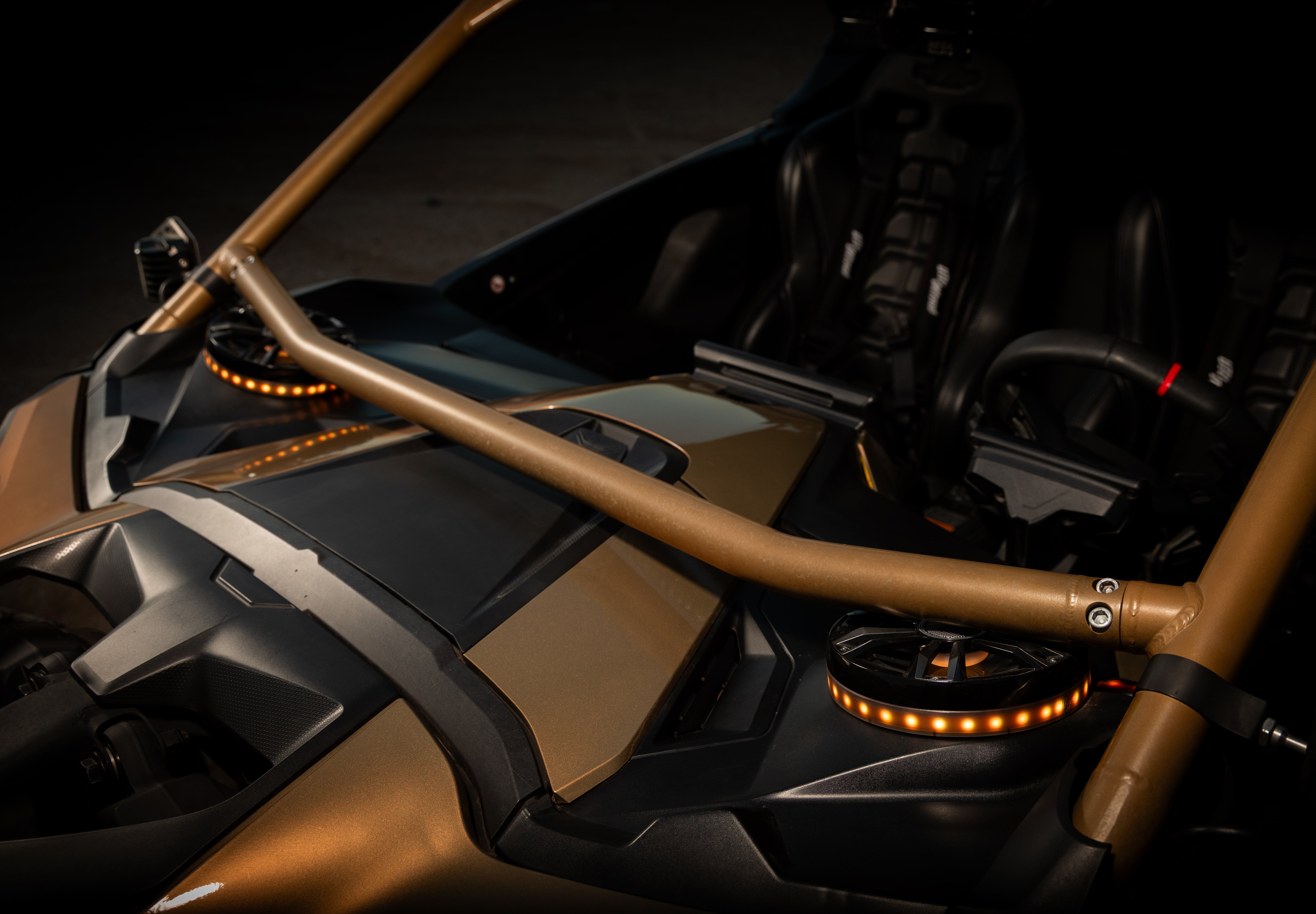 Close-up of a roll cage installed on a black and metallic gold off-road vehicle, with amber LED light accents visible in a dark studio setting.