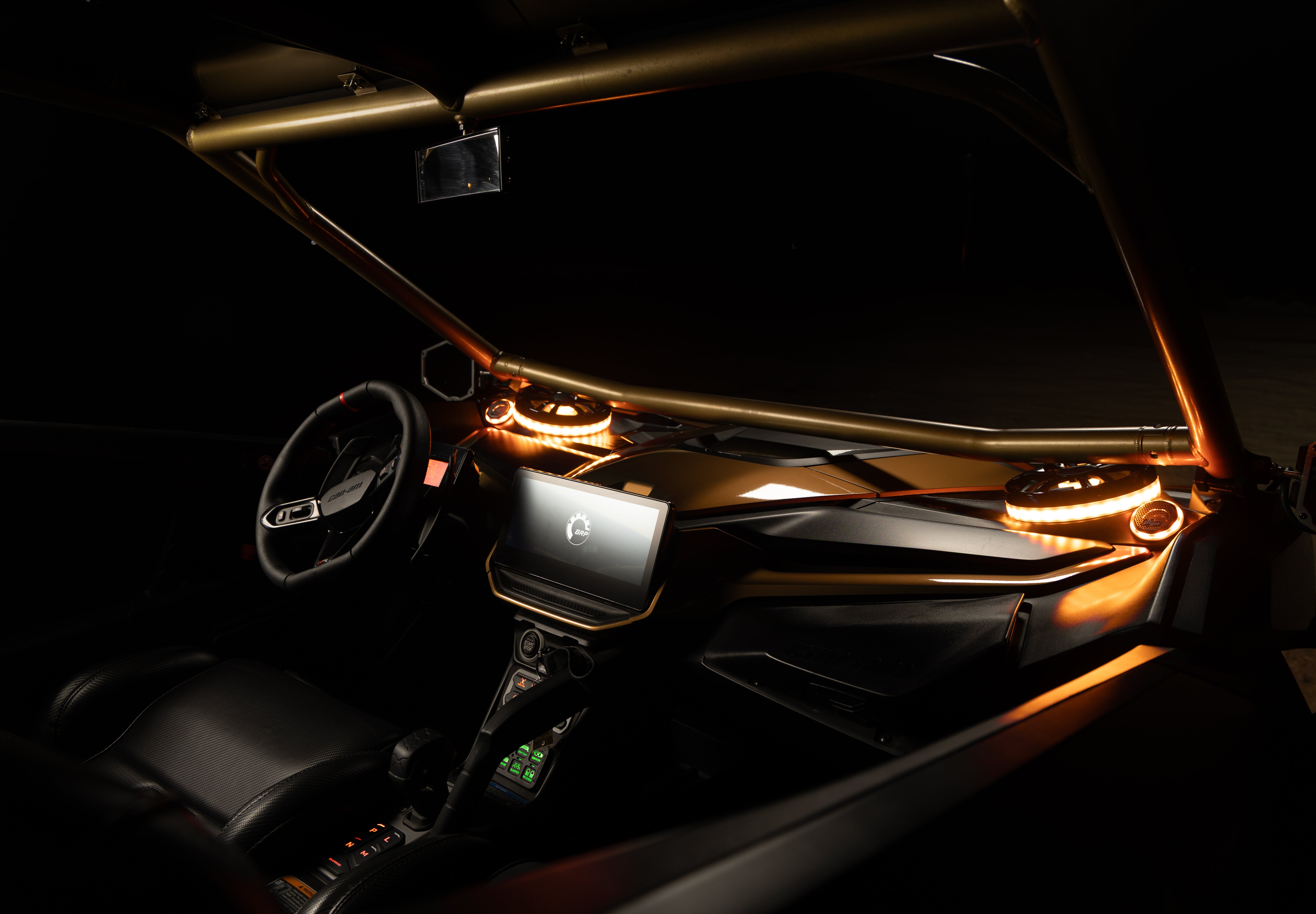 A luxury vehicle interior with a matte black dashboard, gold roll bar, and warm amber LED accent lighting around the screen and cup holders.
