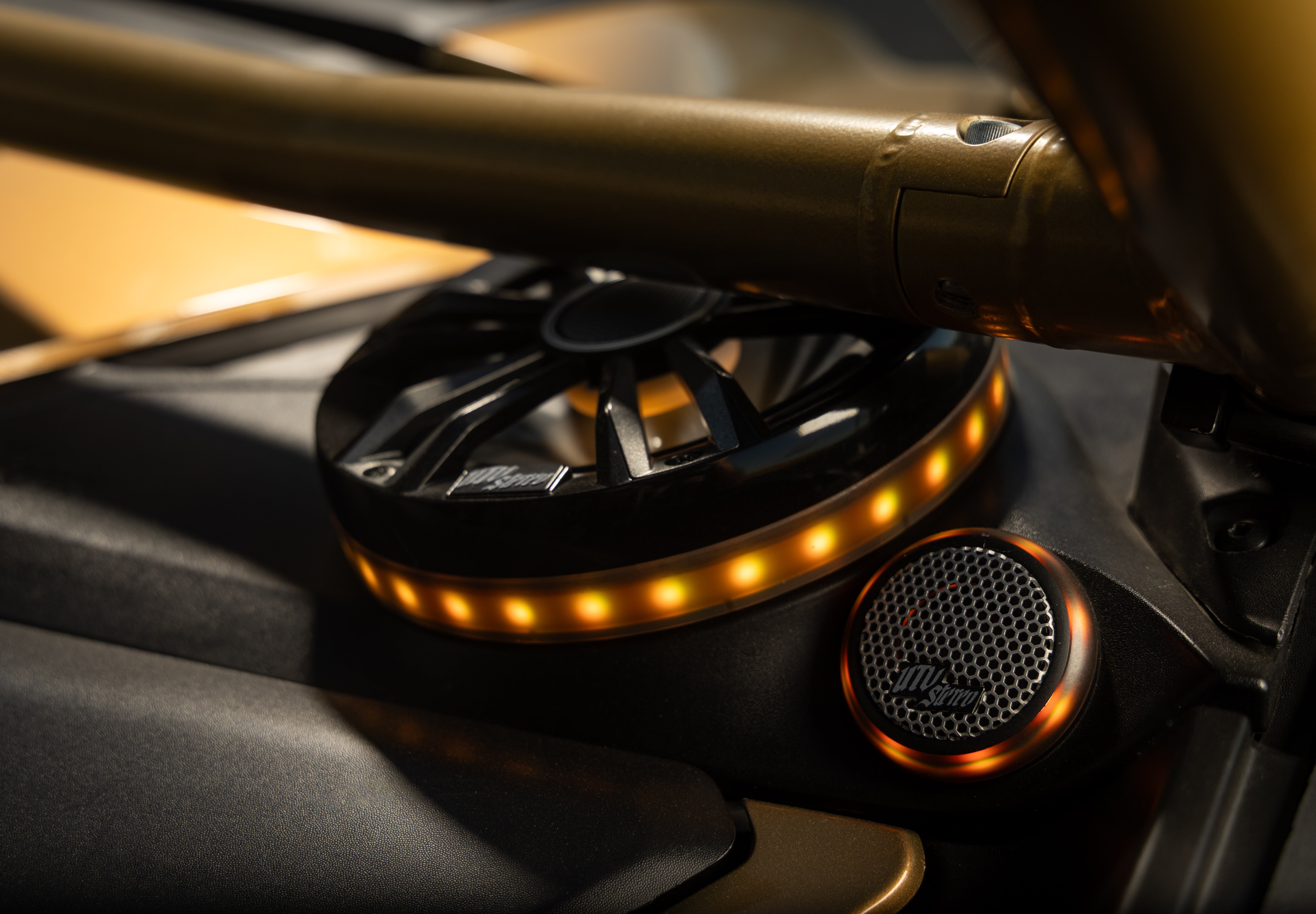 Close-up of a custom car audio speaker setup featuring a circular black speaker with a warm amber LED light ring and a matching round grille.